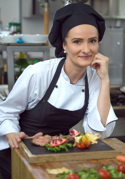 female Chef in restaurant kitchen preparing beef steak with vegetable decoration - Photo, Image