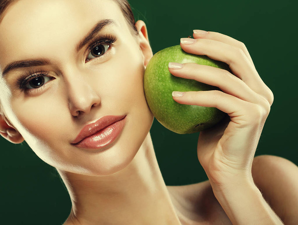 Head shot of woman holding green apple against green background - Zdjęcie, obraz