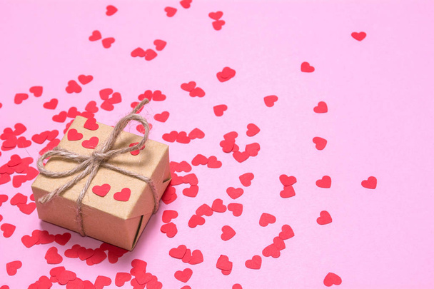 Egy ajándékot csomagolni nátronpapír, egy rózsaszín háttér. Piros szív, egy ajándék doboz. - Fotó, kép