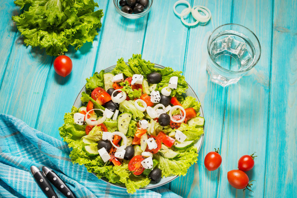 Ensalada griega tradicional con verduras frescas, queso feta y aceitunas sobre fondo de madera azul
 - Foto, imagen