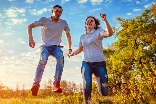 Молодий чоловік і жінка бігають і стрибають. Пара розважається у весняному полі на заході сонця. Хлопці сміються
 - Фото, зображення