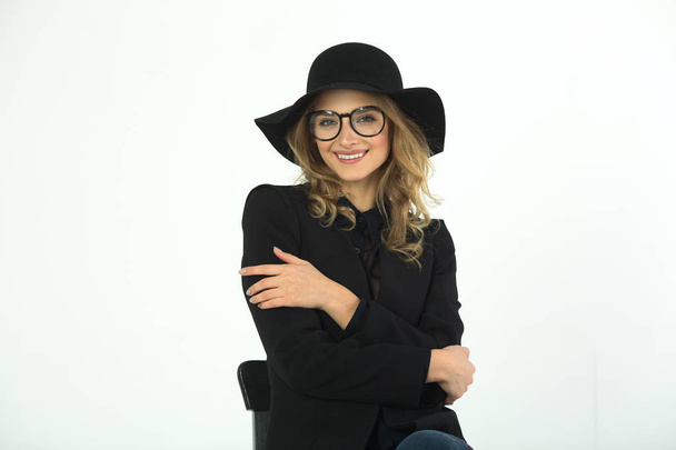 beautiful young girl with glasses and hat, wearing a black jacket on a white background - Fotó, kép