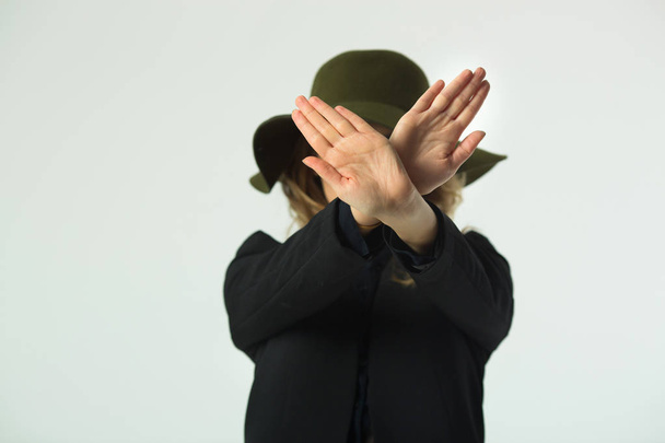beautiful young girl in a hat on a white background with a gesture of a hand signifying a stop - Valokuva, kuva