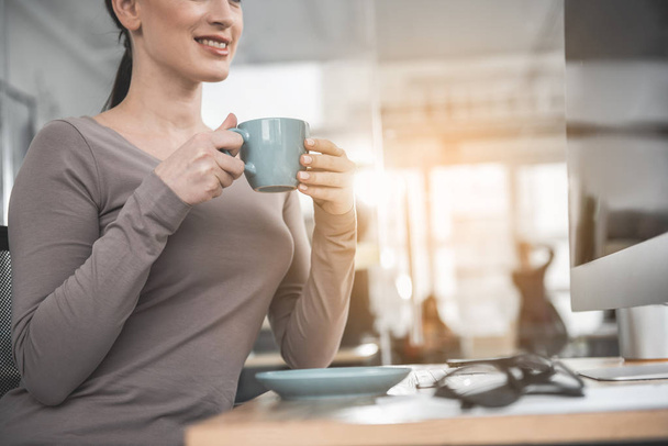 Glad woman tasting cup of coffee at job - Foto, Imagen
