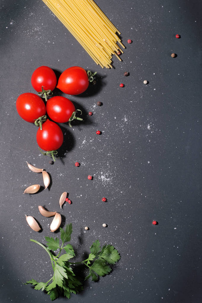 Dry pasta on a black background with a sprig of parsley, cherry tomatoes, pepper and garlic. - Photo, Image