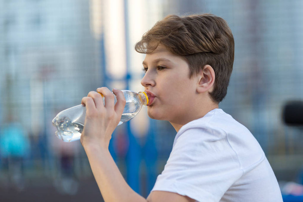 sporty cute boy drinks water after playing basketball on the sports ground. healthy lifestyle concept - Fotó, kép