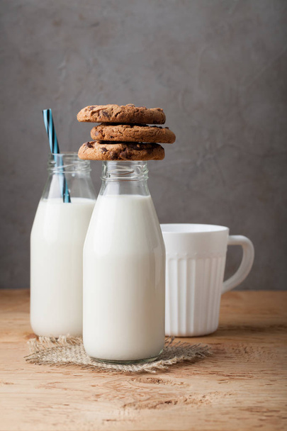 Uma pilha de biscoitos com chocolate ao leite e duas garrafas de leite em uma mesa de madeira
 - Foto, Imagem