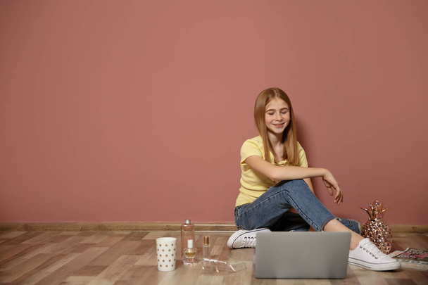 Cute teenage blogger with laptop sitting on floor against color wall - Foto, afbeelding