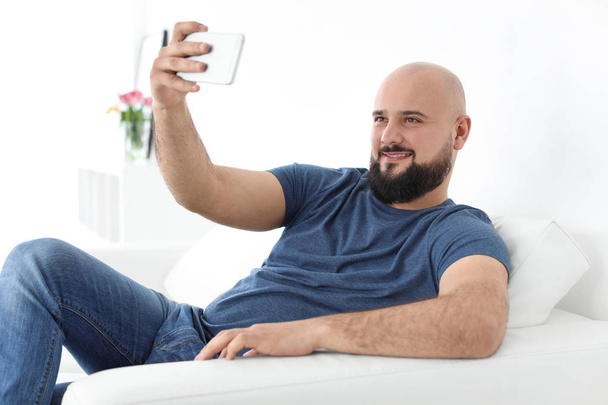 Portrait of young man taking selfie on sofa - Fotoğraf, Görsel