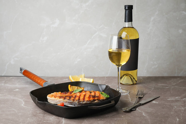 Frying pan with tasty salmon steak and wine on table - 写真・画像