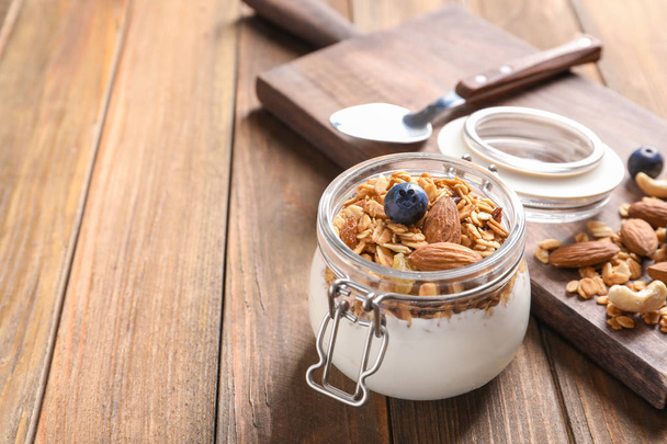 Jar with yogurt, nuts and granola on wooden table - Foto, Imagem
