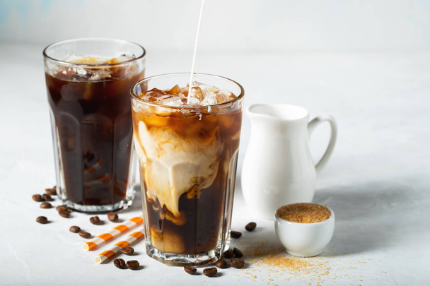Ice coffee in a tall glass with cream poured over and coffee beans. Cold summer drink on a light blue background - Foto, Imagen