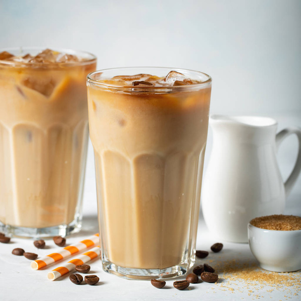 Ice coffee in a tall glass with cream poured over and coffee beans. Cold summer drink on a light blue background - 写真・画像