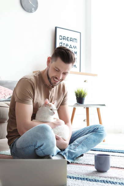 Νεαρός άνδρας με το χαριτωμένο γάτα και φορητό υπολογιστή στο σπίτι - Φωτογραφία, εικόνα
