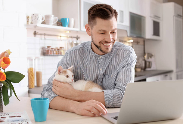 Young man with cute cat and laptop at home - Valokuva, kuva