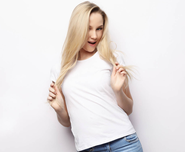 lifestyle and people concept - Beautiful happy blond girl touches her hair. Casual clothes. White background. - Fotó, kép