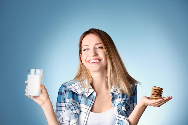 Beautiful young woman drinking milk with cookies on color background - Photo, Image