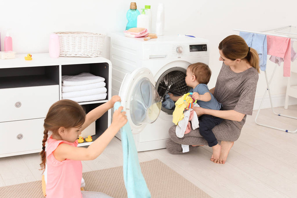 Housewife with little children doing laundry at home - 写真・画像
