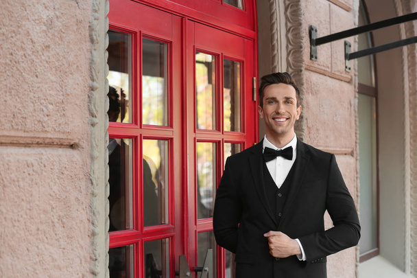 Young doorman in elegant suit standing near restaurant entrance - Fotoğraf, Görsel