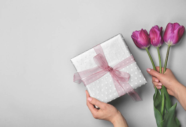 Woman holding elegant gift box and tulips for Mother's Day on light background, top view - Fotoğraf, Görsel
