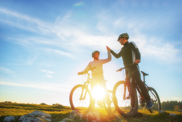 happy couple goes on a mountain road in the woods on bikes with helmets giving each other a high five - 写真・画像