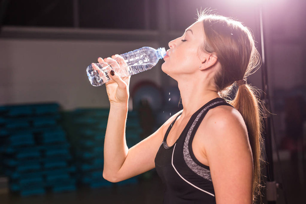 Fitness young woman drinking water in the gym. Muscular woman taking break after exercise - Photo, Image