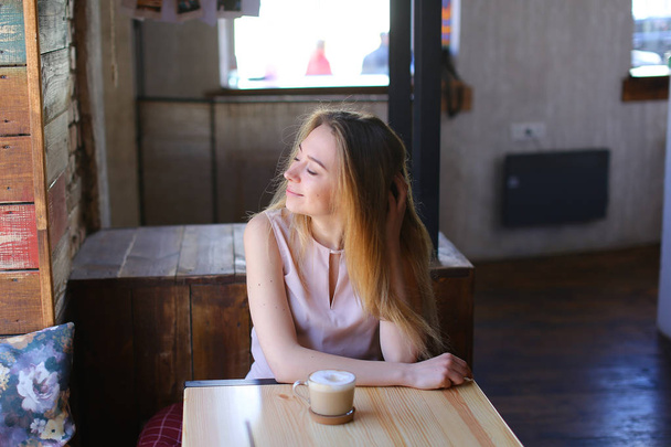 Συλλογισμένος κορίτσι κάθονται με καφεδάκι κοντά στο τραπέζι στην καφετέρια με ωραία ατμόσφαιρα. - Φωτογραφία, εικόνα