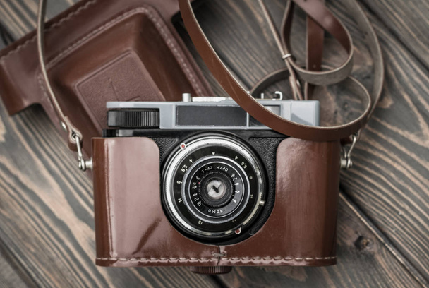Old film camera in a brown leather case against a wooden plank background - Foto, immagini