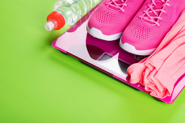 pink sport sneakers and a vest on the scales, and a bottle of water, on a light green background - Фото, зображення