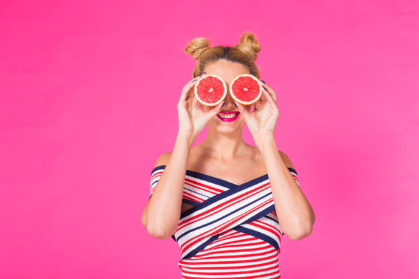Χαμογελαστό κορίτσι με γκρέιπφρουτ κομμένα σε μισά φρούτα στο χέρι σε ροζ φόντο με copyspace - Φωτογραφία, εικόνα