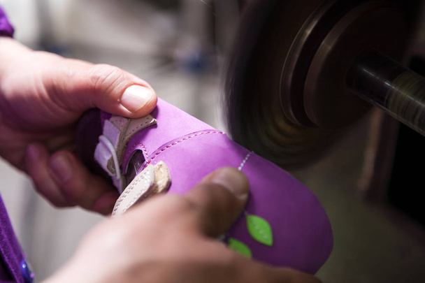 Крупным планом молодой работник мужского пола делает подошву детской обуви из натуральной кожи со специальной машиной в швейной мастерской
 - Фото, изображение