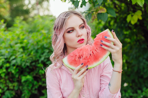 Beautiful young woman with pink hair enjoying watermelon - Fotó, kép