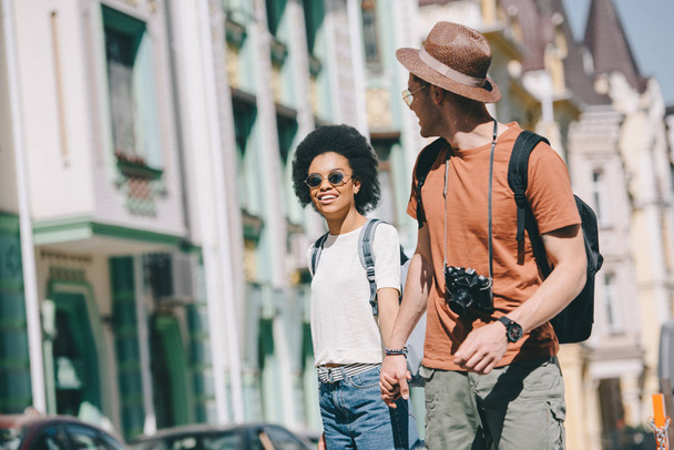 homem viajante com câmera segurando mão de afro-americano namorada
  - Foto, Imagem