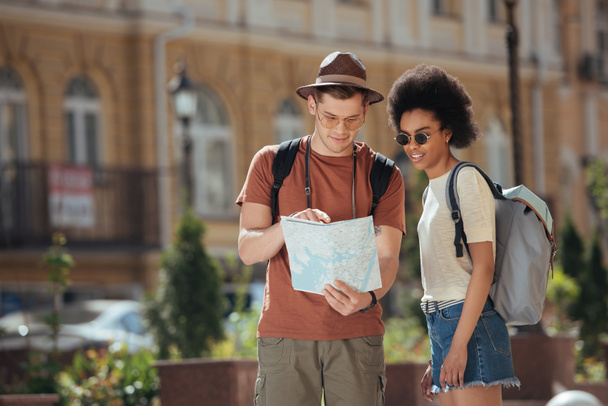 young male traveler pointing at map to african american girlfriend standing near  - Photo, Image