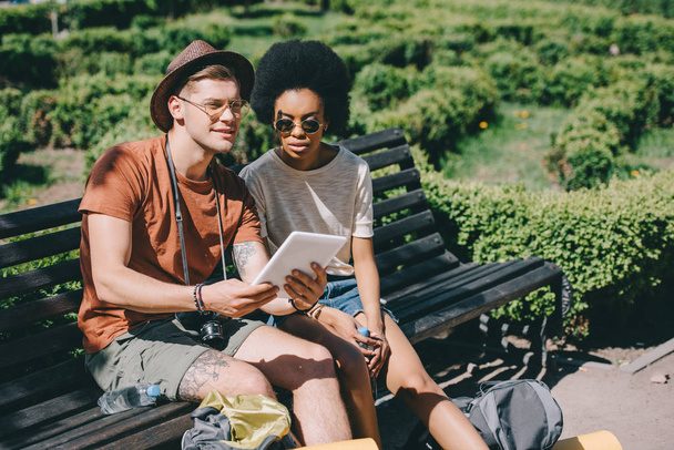 multiethnic couple of young tourists sitting on bench with digital tablet  - Foto, immagini