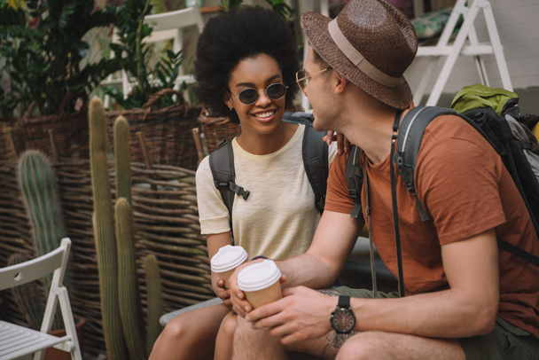 stylish interracial couple sitting with paper cups of coffee  - Zdjęcie, obraz