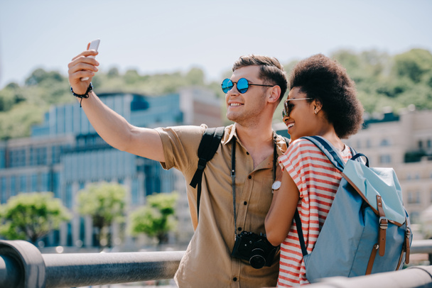 multiethnic couple of travelers in sunglasses taking selfie on smartphone  - Photo, Image