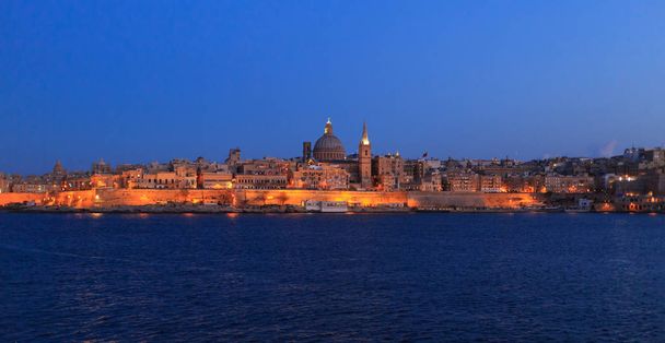 Valletta, Malta in the evening. Panoramic view of illuminated historic island and the dome of Carmelite Church and St Paul`s tower. - Photo, Image