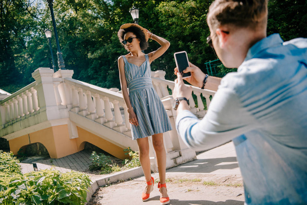 man taking picture of stylish african american woman on smartphone in park  - Fotó, kép