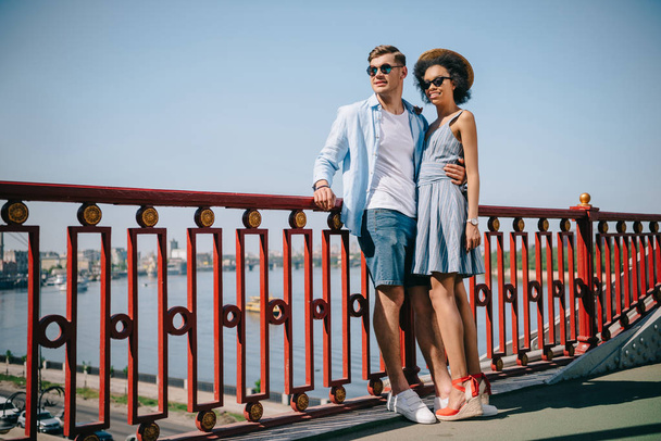 stijlvolle multi-etnisch paar in zonnebril permanent op brug  - Foto, afbeelding