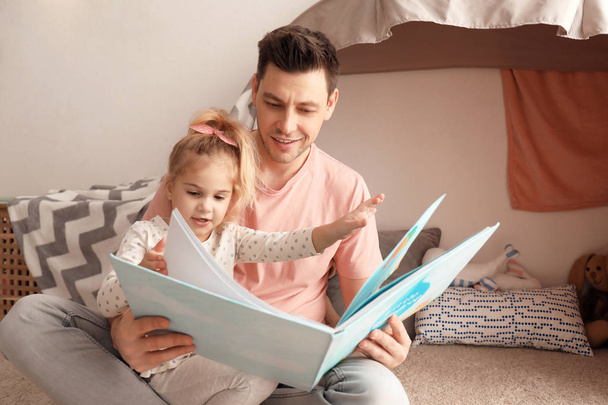 Father and his daughter reading book in children room - Photo, Image