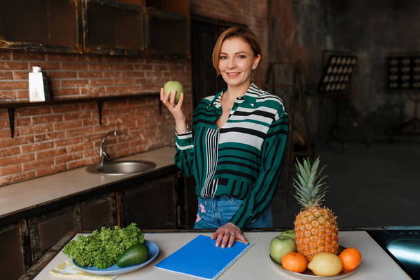 Чудова здорова молода жінка їсть яблуко на сучасній кухні. Фітнес-тренер. З'їж право, щоб тримати животик міцно
 - Фото, зображення