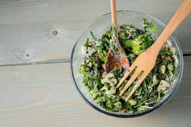 close-up photo of fresh green salad with arugula and spinach in bowl on table with wooden fork and spoon - Photo, Image