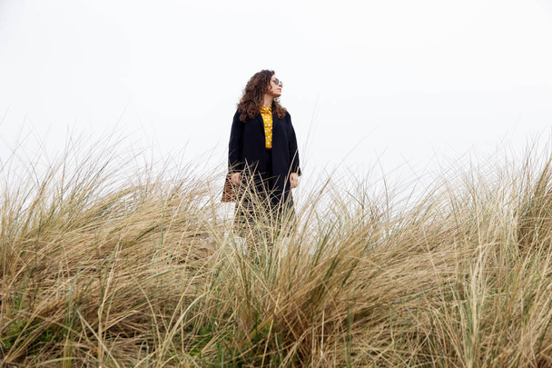 Girl rain sea wind portrait woman spring coat long hair curly mood shore beach dry grass sky - Fotoğraf, Görsel