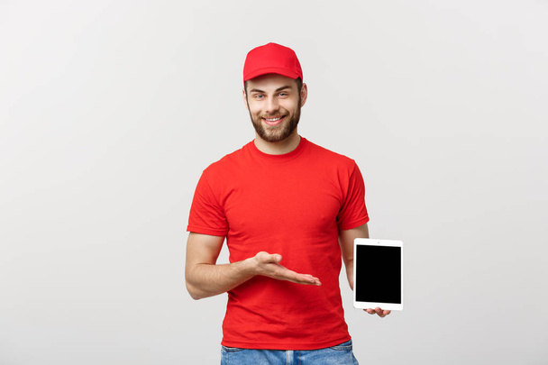 Online shopping, delivery, technology and lifestyle concept - smiling delivery man presenting tablet in his hand showing something. Isolated over white studio background. - Fotoğraf, Görsel