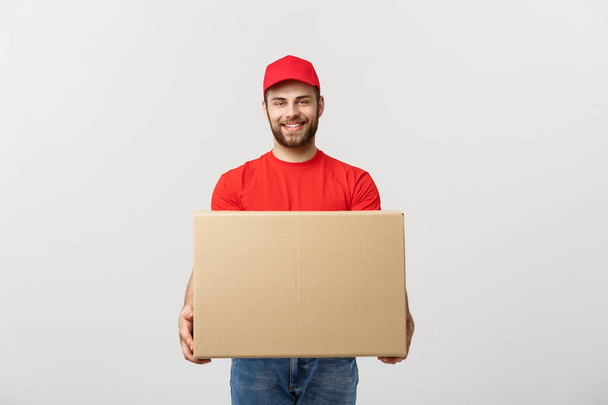 Jeune livreur logistique souriant en uniforme rouge tenant la boîte sur fond blanc
 - Photo, image