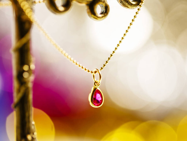 golden necklace with ruby on colorful background. - 写真・画像