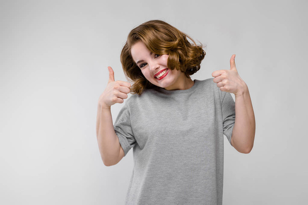 Charming young girl in a gray T-shirt on a gray background. Girl showing class sign - Fotó, kép