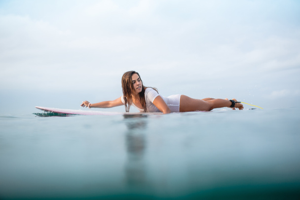 beautiful young woman swimming on surfboard in ocean - Photo, Image