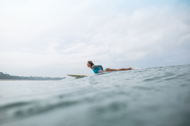 side view of sportive young woman riding on surfboard in ocean - Foto, imagen